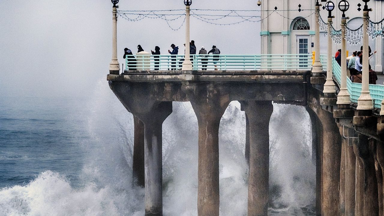 People stand at the end of the Manhattan Beach Pier and watch high surf pound the pylons on Tuesday, Dec. 24, 2024 in Manhattan Beach, Calif. (AP Photo/Richard Vogel)