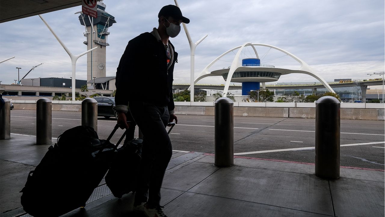 A holiday traveler wearing a face mask arrives at the Los Angeles International Airport in Los Angeles, Dec. 22, 2021. (AP Photo/Ringo H.W. Chiu)