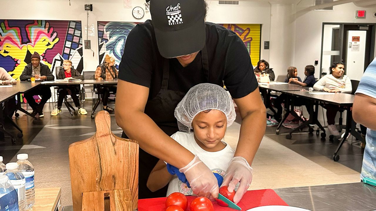 Chef Sharrie Agee helps Yareni Orduna-Herrera slice tomatoes for a margherita pizza as part of the Milwaukee Public Library Snack Hack