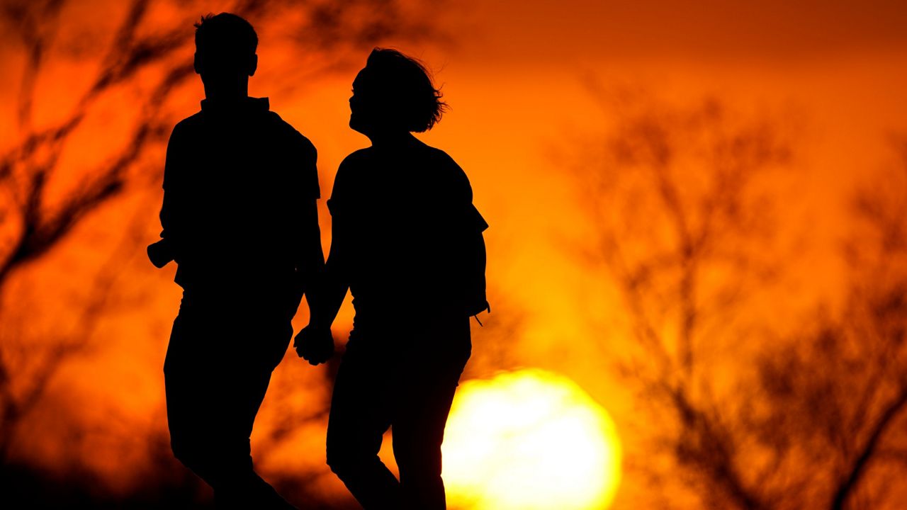 A couple walks through a park at sunset in Kansas City, Mo. (AP Photo/Charlie Riedel, File)