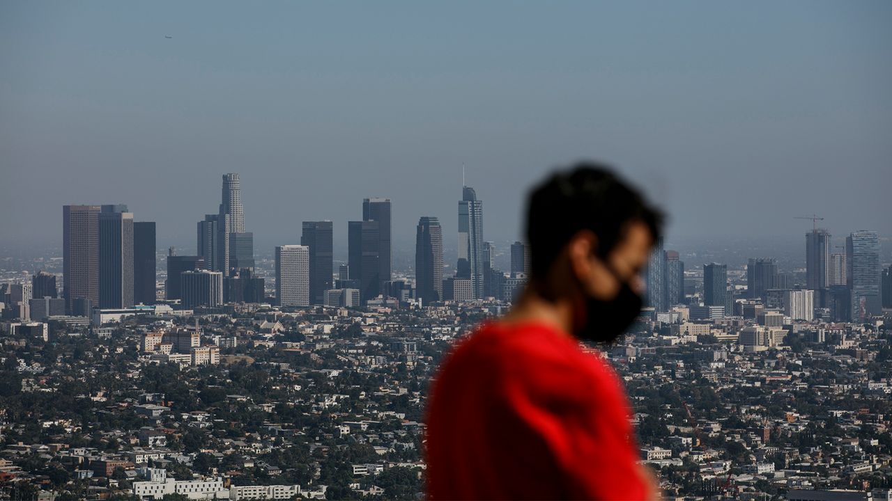 Image shows Izzy Galvan, 20, wears a face mask while visiting the Griffith Observatory overlooking downtown Los Angeles