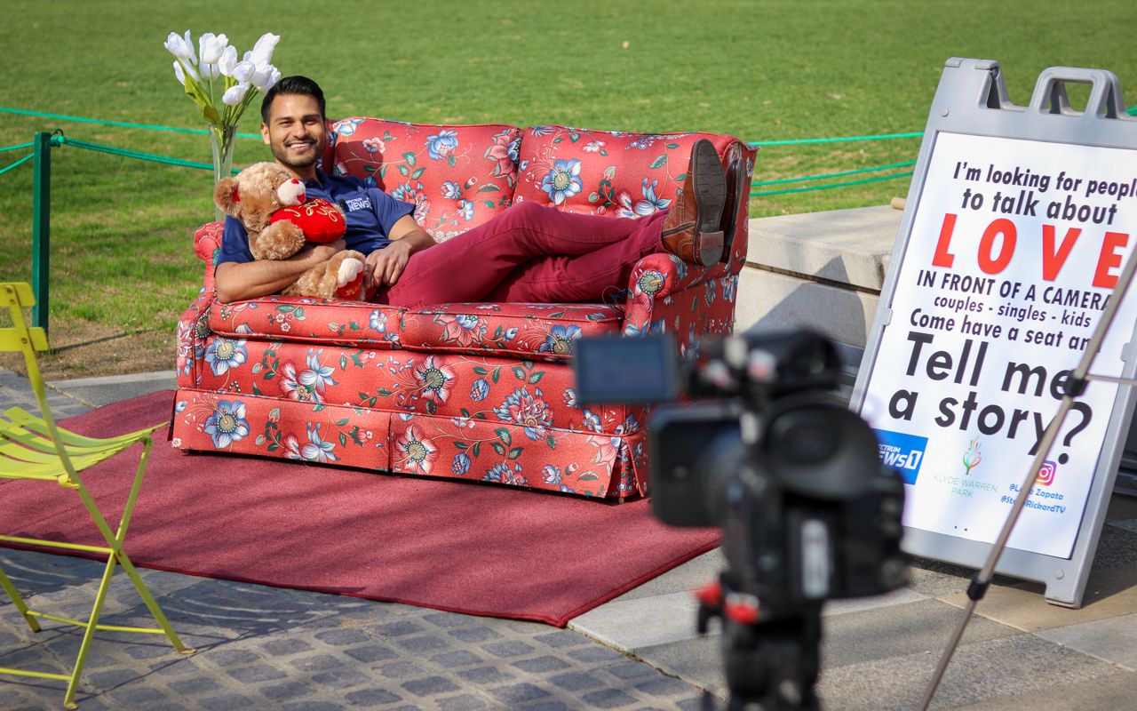 Pictured is Spectrum reporter Lupe Zapata and a sign that reads “I’m looking for people to talk about love” used to while filming “Tell Me A Story,” produced by Zapata and Dallas reporter Stacy Rickard for Spectrum News 1 Texas. (Stacy Rickard/Spectrum News 1)