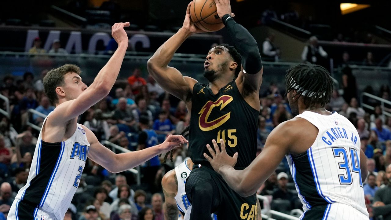 Cleveland Cavaliers' Donovan Mitchell (45) makes a shot as he gets between Orlando Magic's Franz Wagner, left, and Wendell Carter Jr. (34) during the first half of an NBA basketball game, Tuesday, April 4, 2023, in Orlando, Fla.