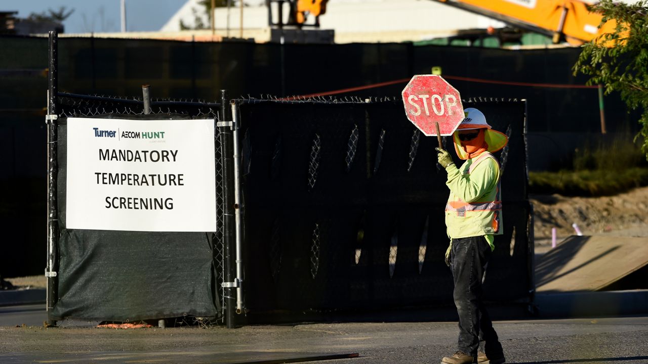 A worker directs traffic near a sign calling for mandatory temperature checks of workers at a construction site near the new SoFi Stadium, Thursday, April 23, 2020, in Los Angeles. (AP Photo/Chris Pizzello)