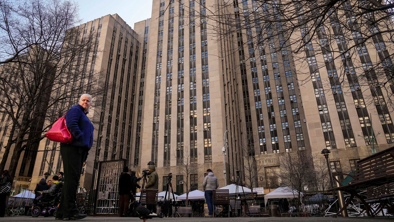 Pedestrians stand outside Manhattan Criminal Court as media and security amass nearby, Monday, April 3, 2023, in New York. Former President Donald Trump is expected to travel to New York to face charges related to hush money payments. Trump is facing multiple charges of falsifying business records, including at least one felony offense, in the indictment handed up by a Manhattan grand jury. (AP Photo/John Minchillo)