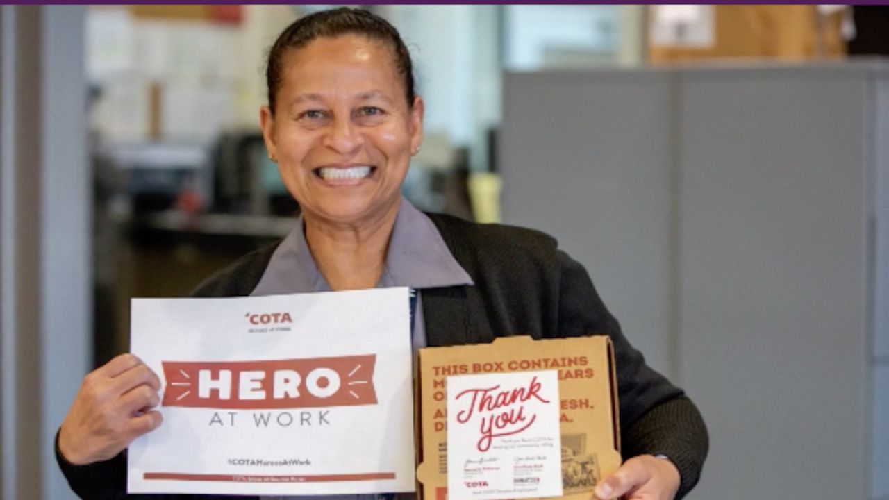 Woman holding a white pizza box that says Hero At Work and a small brown pizza box that says Thank You