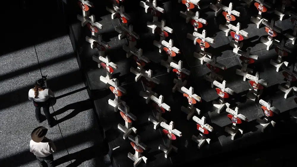 In this Sept. 25, 2018, photo, people look at a display of wooden crosses and a Star of David on display at the Clark County Government Center in Las Vegas. It was the deadliest mass shooting in modern U.S. history on the Las Vegas Strip in 2017. More than 100 people have been killed in mass shootings thus far in 2023, an average of one mass killing a week. (AP Photo/John Locher, File)-