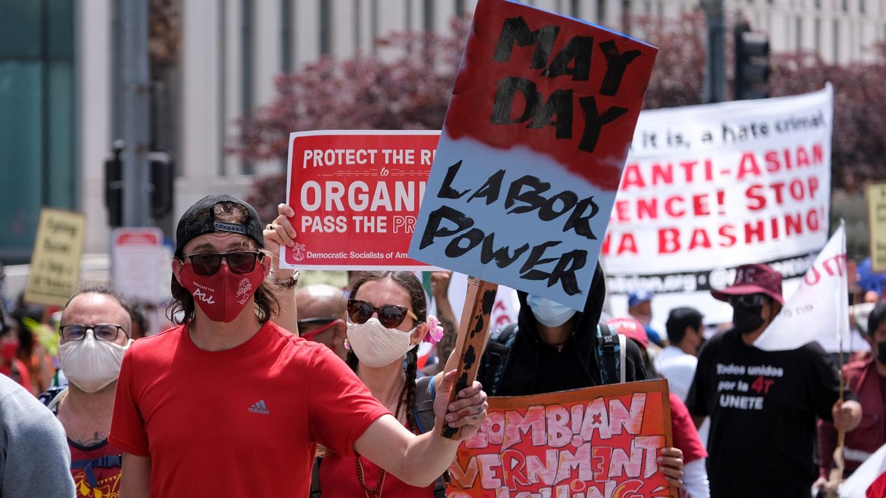 People wearing face masks and holding signs take part in the annual May Day marches on May 1, 2021, in downtown Los Angeles. (AP Photo/Ringo H.W. Chiu)