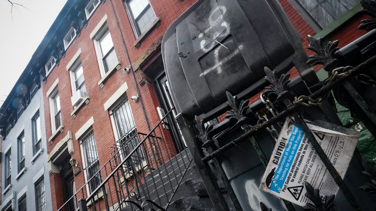 A caution sign for rodenticide is posted on a fence next door to a building, second from left, owned by New York Mayor Eric Adams in the Bedford-Stuyvesant neighborhood of the Brooklyn borough of New York, Dec. 7, 2022. (AP Photo/Bebeto Matthews, file)