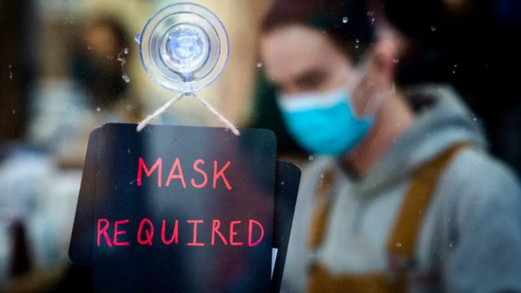 Generic photo of an employee wearing a mask behind a 'Mask Required' sign. (Spectrum Files)