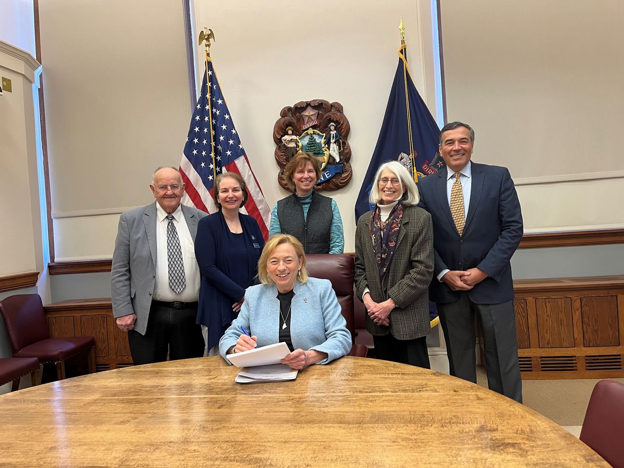 Maine Gov. Janet Mills, seated, has signed a supplemental budget into law.