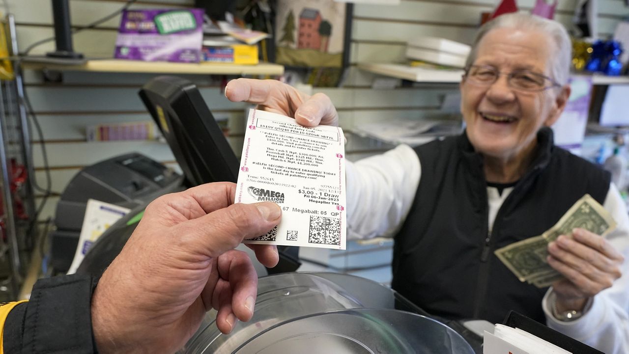 Dot Skoko, owner of Dot's Dollar More or Less shop in Mt. Lebanon, Pa., hands a customer a Mega Millions lottery ticket, Thursday, Jan. 5, 2022. The Mega Millions jackpot has reached an astounding $977 million for Friday night’s drawing after no tickets matched all six numbers drawn on Tuesday night. (AP Photo/Gene J. Puskar, File)