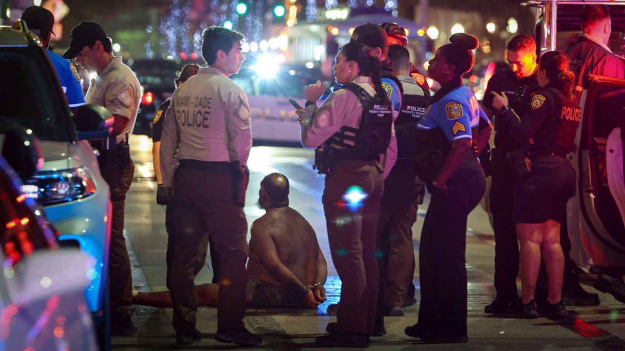 A man sits on the ground handcuffed after witnesses say he appeared to be brandishing a knife on Sunday, March 19, 2023, in Miami Beach, Fla. After three consecutive years of spring break violence, including two fatal shootings last year, Miami Beach officials announced a series of measures to curb non residents from coming to Miami Beach. (Alie Skowronski/Miami Herald via AP, File)