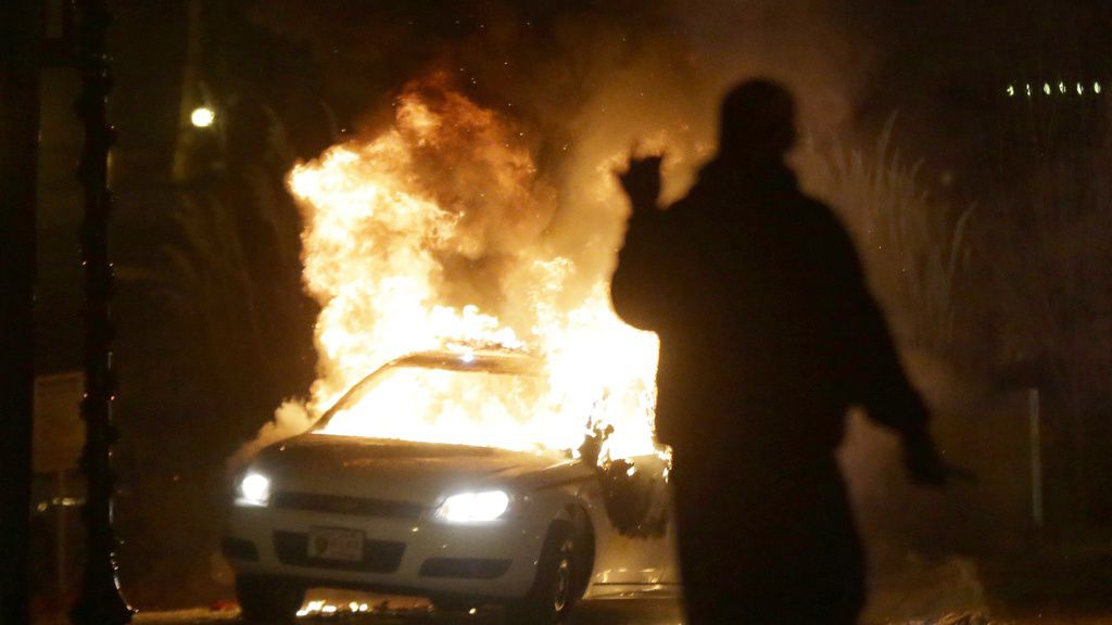 A police car is set on fire in the fallout surrounding Michael Brown's death in 2014. The city of Florissant, Mo., will pay nearly $3 million to settle a so-called debtor's prison lawsuit that accused the city of violating the constitutional rights of residents. (AP Photo/Charlie Riedel, File)