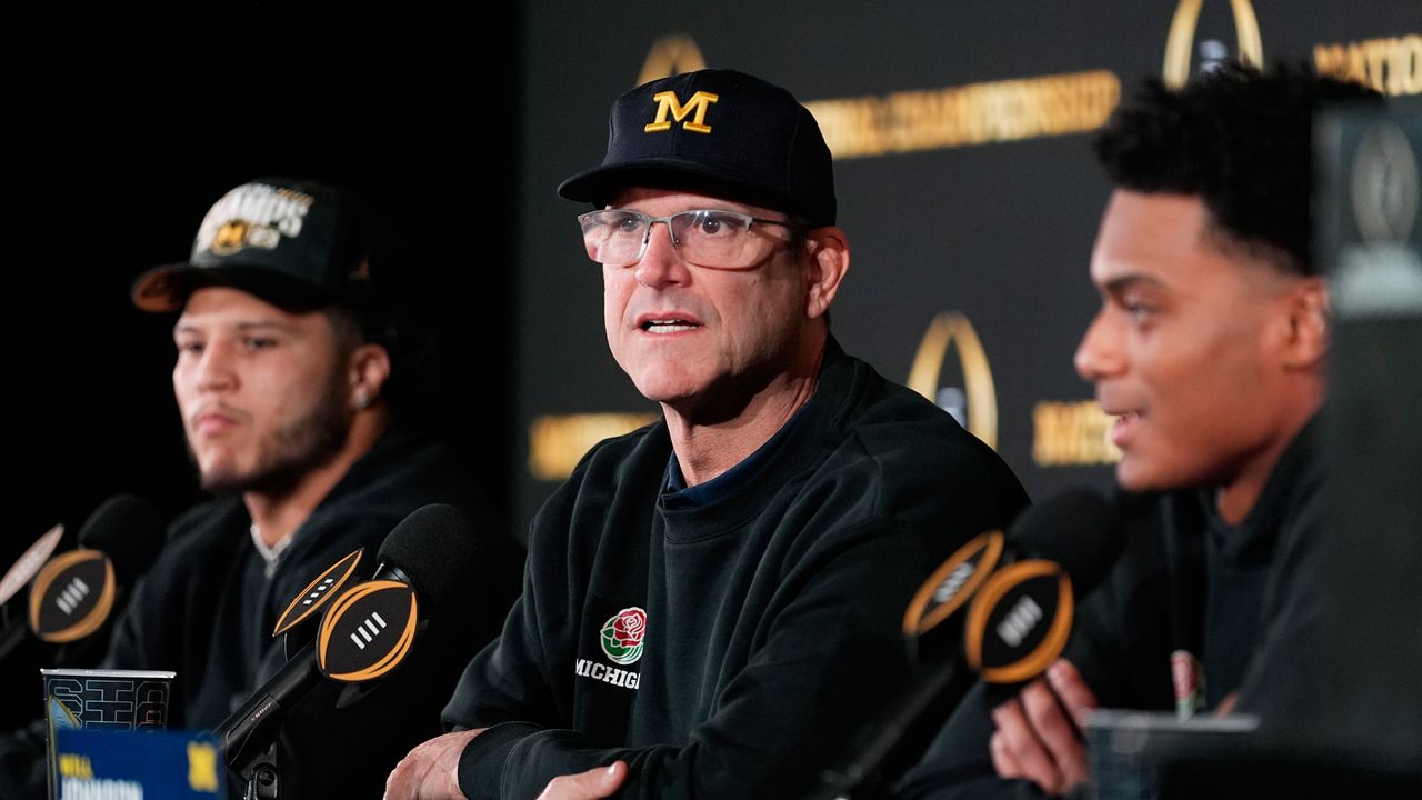 Michigan head coach Jim Harbaugh, center, with running back Blake Corum, left, and defensive back Will Johnson, right, speaks during an NCAA college football news conference Tuesday, Jan. 9, 2024, in Houston.  Harbaugh and No. 1 Michigan completed a three-year climb to a national championship by beating No. 2 Washington 34-13 Monday night in the College Football Playoff title game.