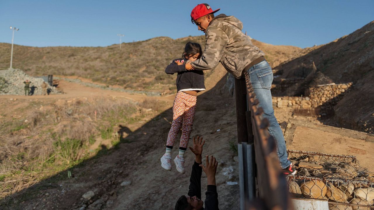 A migrant from Honduras passes a child to her father after he jumped the border fence to get into the U.S. side to San Diego, Calif., from Tijuana, Mexico, on Jan. 3, 2019. (AP Photo/Daniel Ochoa de Olza, File)