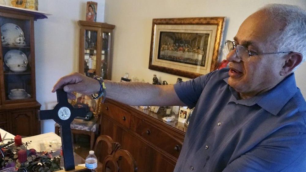 Bob Guerra, a Catholic deacon, holds a crucifix he got to commemorate the visit of Pope Francis to the U.S.-Mexican border at his house in El Paso, Texas, on Sunday, April 3, 2022. Guerra takes the crucifix alongside other liturgical items to help clergy celebrate Mass for hundreds of teens held at a shelter on the Army's Fort Bliss base after crossing the border without parents or guardians. (AP Photo/Giovanna Dell'Orto)