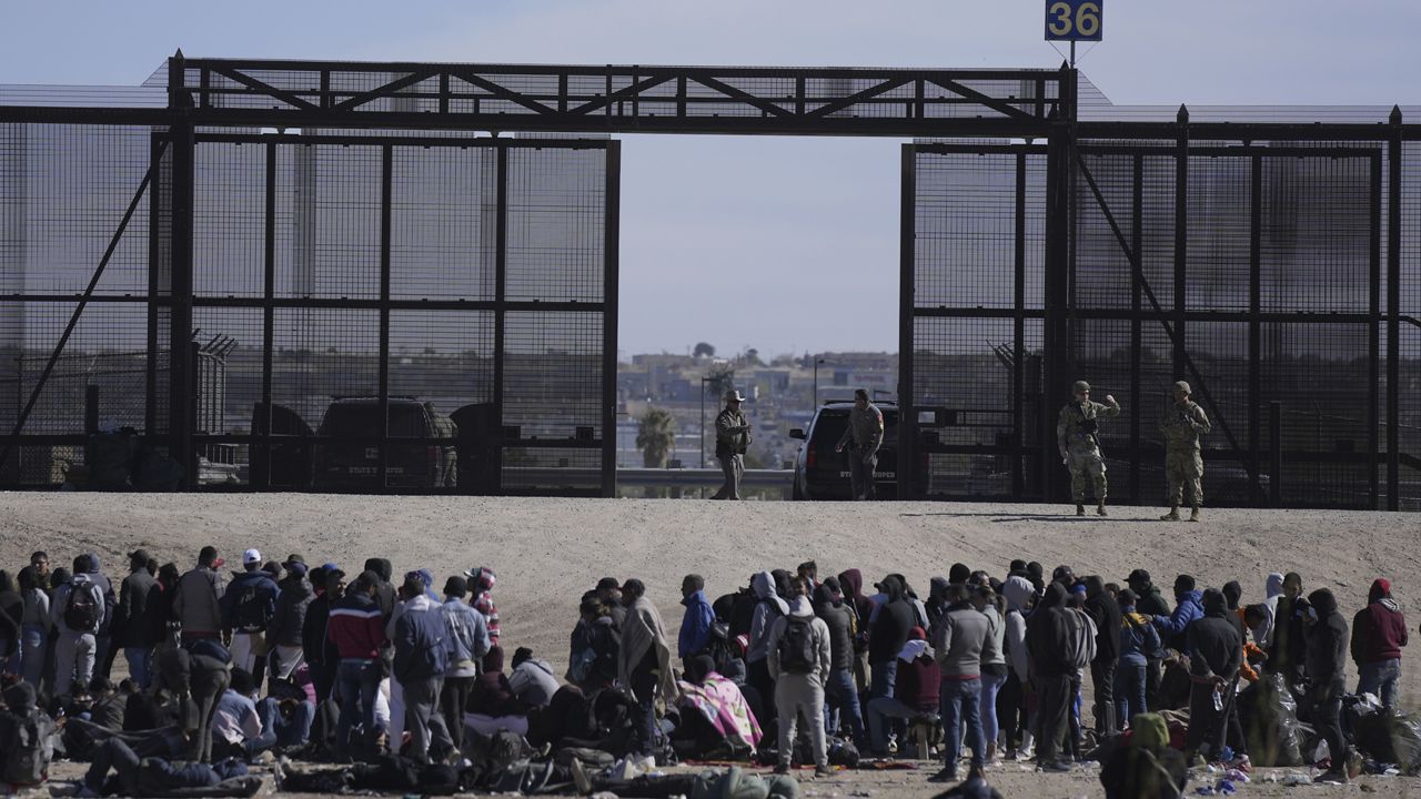 Migrants who crossed the border from Mexico into the U.S. wait next to the U.S. border wall where U.S. Border Patrol agents stand guard, seen from Ciudad Juarez, Mexico, Thursday, March 30, 2023. (AP Photo/Fernando Llano)