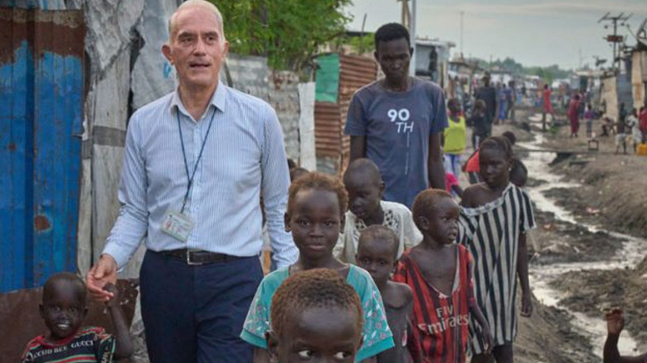 father mike bassano walks dirt road of a foreign city with a number of children in tow