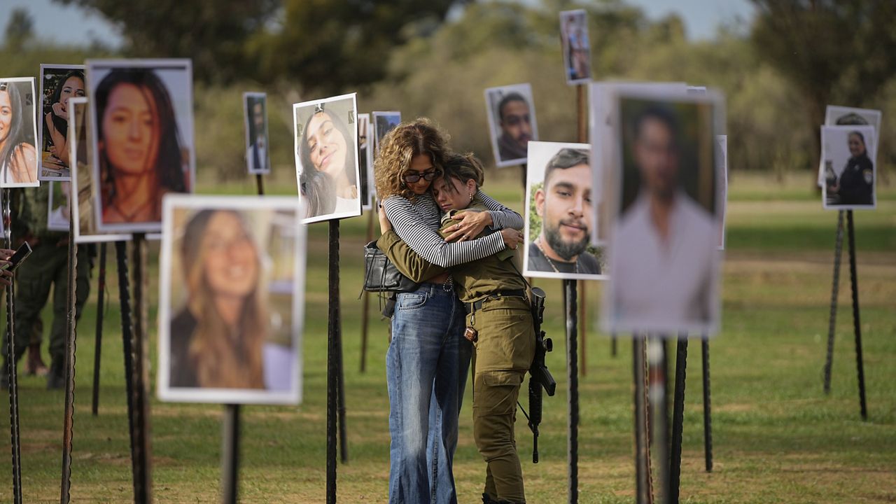 Israelis embrace next to photos of people killed and taken captive by Hamas militants during their violent rampage through the Nova music festival in southern Israel, which are displayed at the site of the event. (AP Photo/Ohad Zwigenberg)