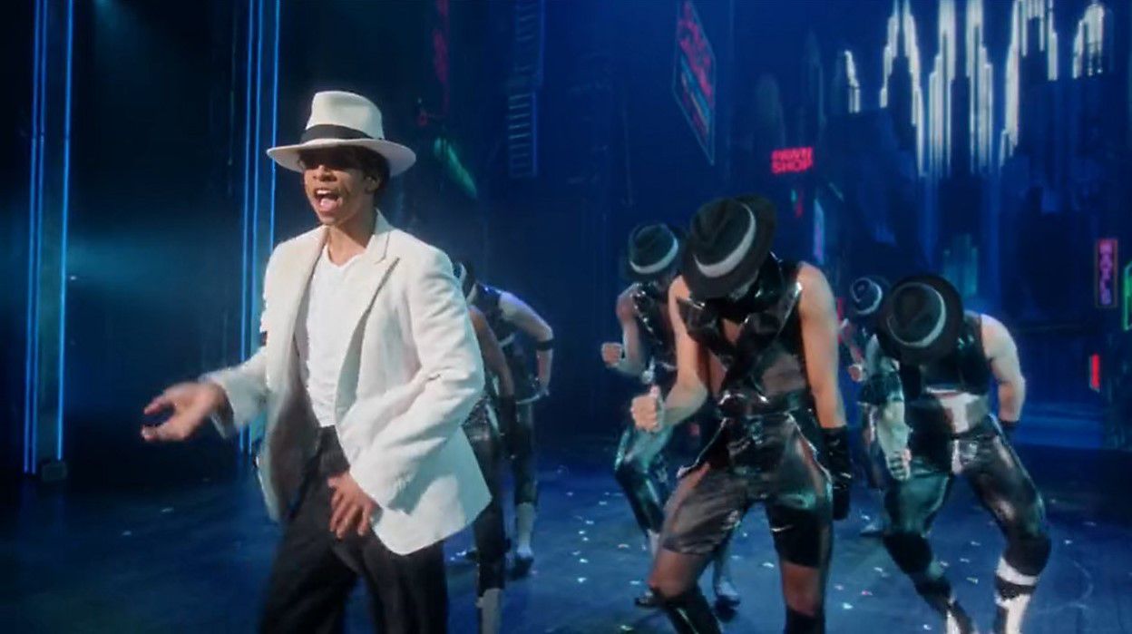 still from michael jackson musical, with actor playing jackson in white suit with backup dancers behind him