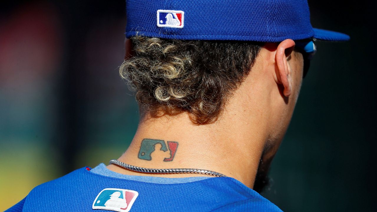 Then-Chicago Cubs' Javier Baez sports an MLB logo tattoo and logos on his hat and jersey as he waits to take batting practice before Game 2 of baseball's National League Division Series against the Washington Nationals at Nationals Park, Saturday, Oct. 7, 2017, in Washington. (AP Photo/Pablo Martinez Monsivais)