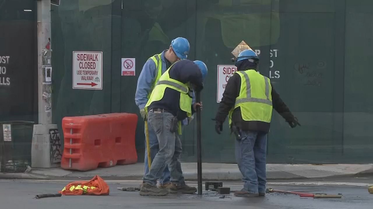 Three construction workers in green vests and hard hats working on the road. 