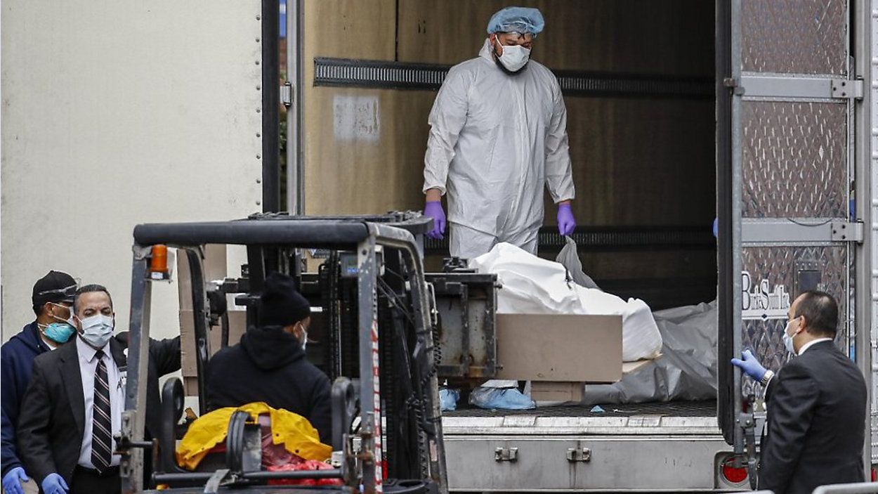 A body wrapped in plastic is loaded onto a refrigerated container truck used as a temporary morgue by medical workers wearing personal protective equipment due to COVID-19 concerns, Tuesday, March 31, 2020. (AP Photo/John Minchillo)
