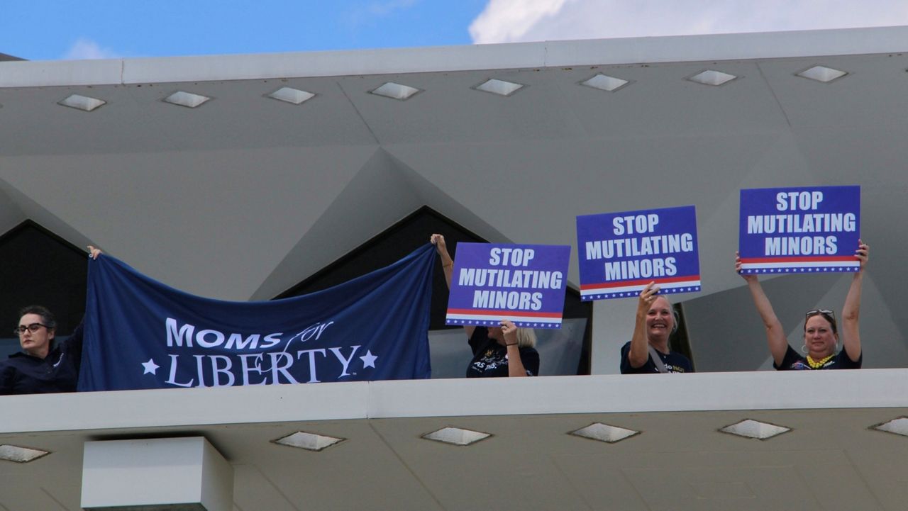 Demonstrators from Moms for Liberty hold protest signs on the roof of the North Carolina Legislative Building, Wednesday, Aug. 16, 2023, in Raleigh, N.C. The state legislature's Republican supermajority will attempt later Wednesday to override the Democratic governor's veto of a gender-affirming care ban for minors. (AP Photo/Hannah Schoenbaum)