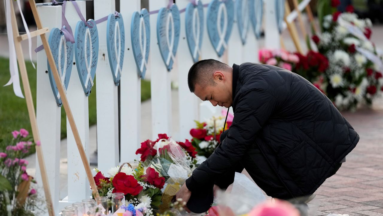 A man lays flowers near wooden hearts displaying names of victims at a vigil outside Monterey Park City Hall, blocks from the Star Ballroom Dance Studio on Tuesday, Jan. 24, 2023, in Monterey Park, Calif. (AP Photo/Ashley Landis)