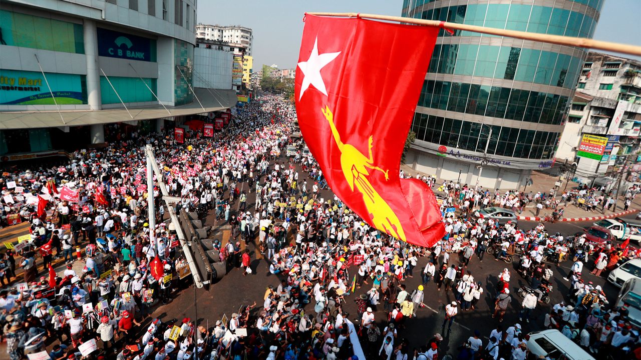 Anti-coup protesters gather outside the Hledan Centre while the flag of the National League for Democracy party is waved from an overhead roadway in Yangon, Myanmar Monday, Feb. 22, 2021. (AP Photo)