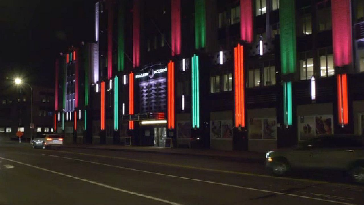 christmas lights lit up at night on national grid building in syracuse, with cars driving by