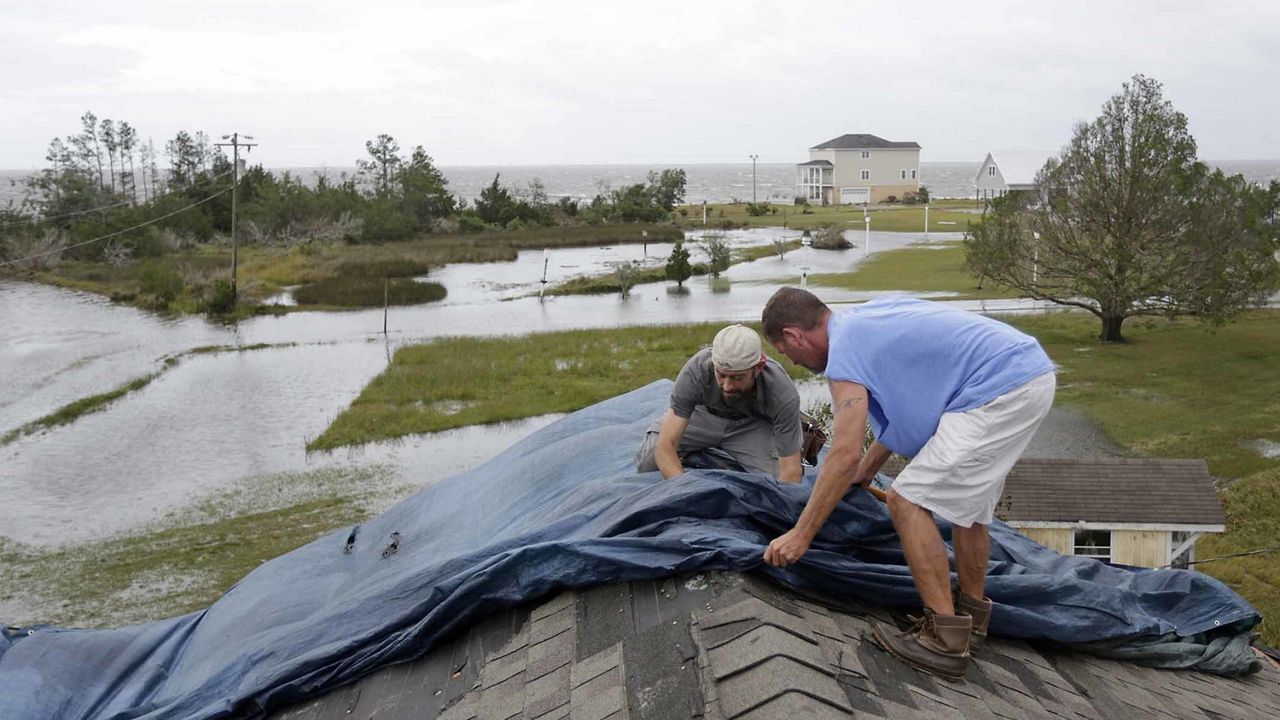 Jeff Pyron, left, and Daniel Lilly cover Lilly's roof after Hurricane Florence hit Davis N.C., Saturday, Sept. 15, 2018. The town had 4 1/2 feet of storm surge. "I had my house raised for Irene cause I got flooded from the bottom, now i'm getting flooded from the top," Lilly said. (AP Photo/Tom Copeland)