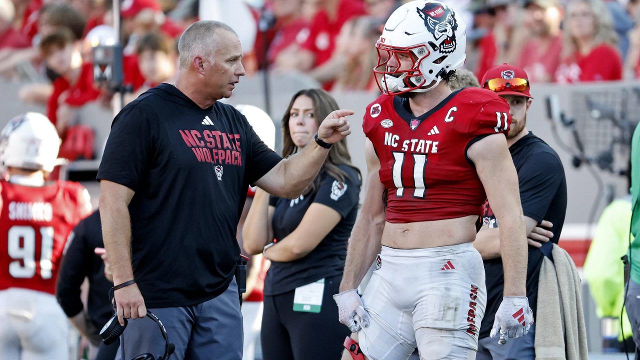 North Carolina State head coach Dave Doeren, left, speaks with North Carolina State linebacker Payton Wilson wearing a knee brace following an injury during the second half of an NCAA college football game against Clemson in Raleigh, N.C., Saturday, Oct. 28, 2023. (AP Photo/Karl B DeBlaker)