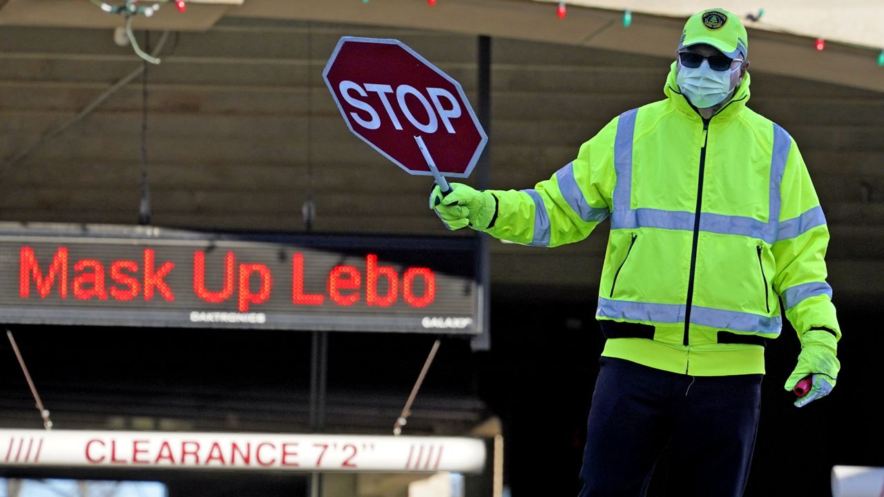 A school crossing guard works in Mount Lebanon, Pa., in front of a sign reminding people to wear a mask, Wednesday, Nov. 18, 2020. (AP Photo/Gene J. Puskar)