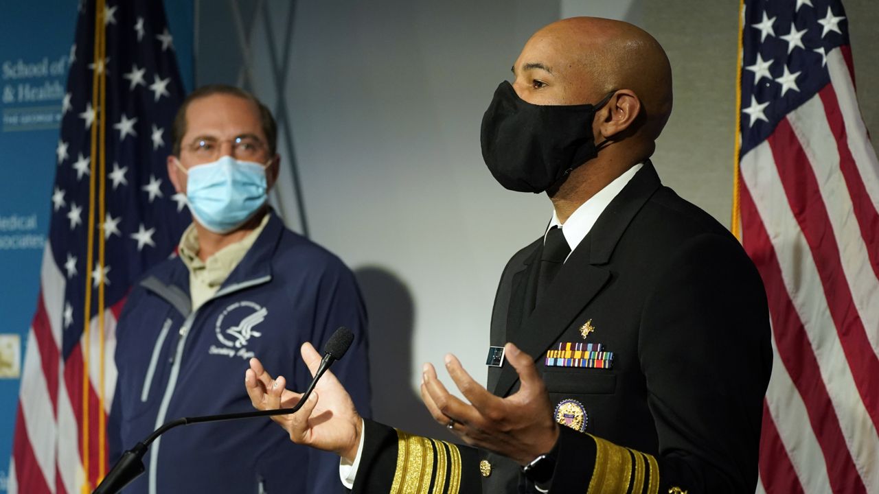 U.S. Surgeon General Dr. Jerome Adams speaks at George Washington University Hospital, Monday, Dec. 14, 2020, in Washington, as Health and Human Services Secretary Alex Azar listens. The two spoke before watching COVID-19 vaccines being administered. (AP Photo/Jacquelyn Martin, Pool)