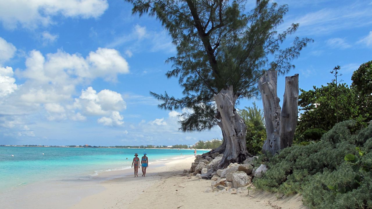 FILE - In this Aug. 3, 2012 file photo, tourists walk along the shore of Seven Mile Beach in Grand Cayman Island.  (AP Photo/David McFadden, File)