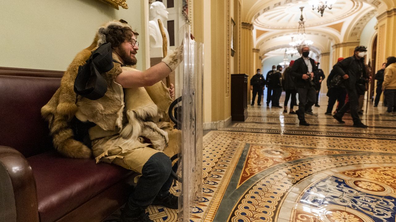 A supporter of President Donald Trump takes a seat holding a shield outside the Senate Chamber on Wednesday, Jan. 6, 2021 in Washington. (AP Photo/Manuel Balce Ceneta)