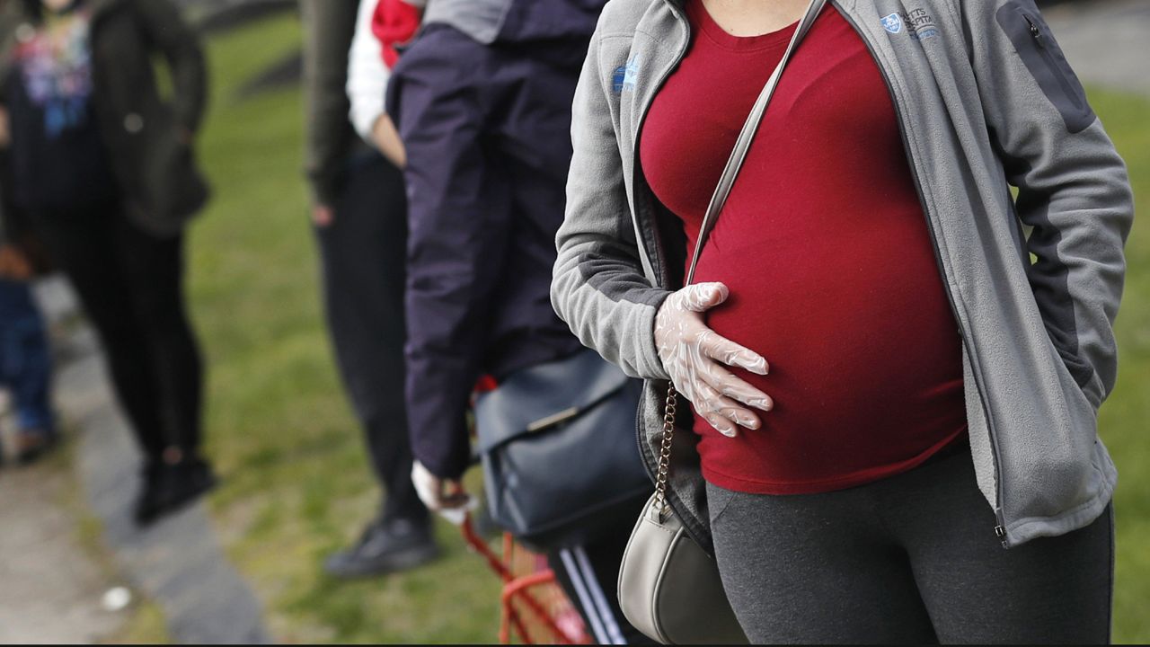 FILE - In this Thursday, May 7, 2020 file photo, a pregnant woman wearing a face mask and gloves holds her belly. (AP Photo/Charles Krupa)