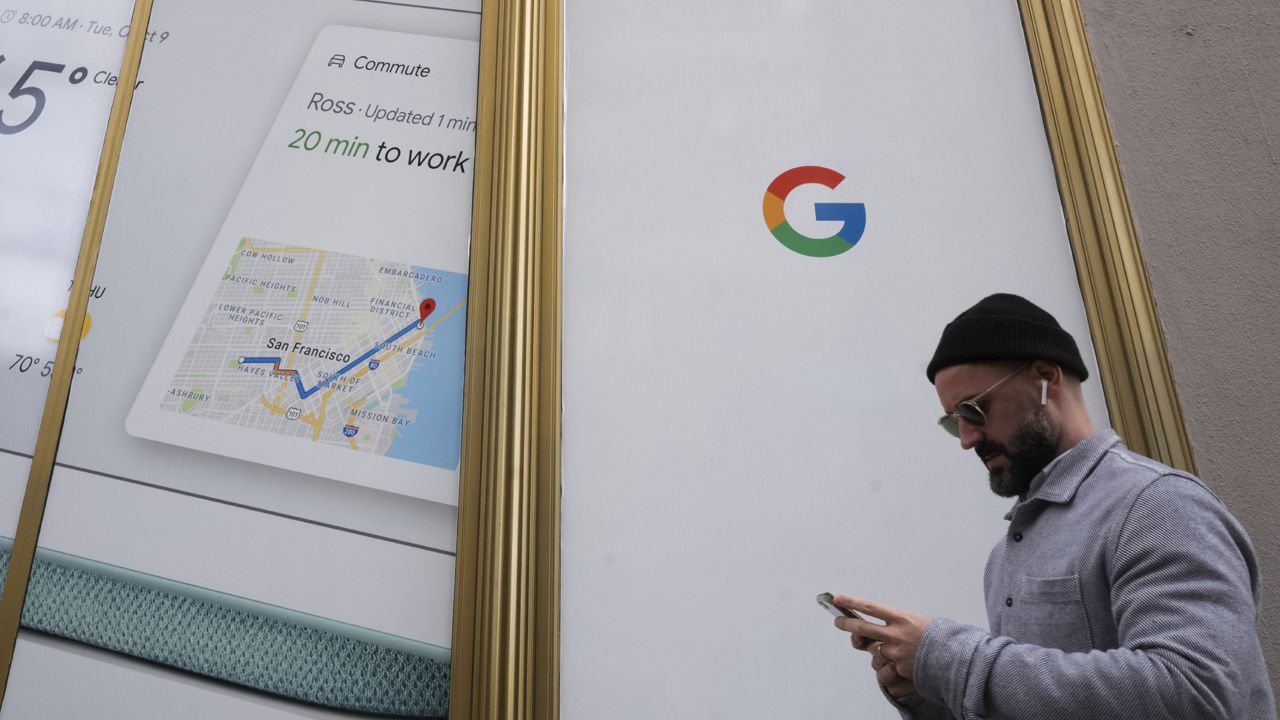 FILE: A man using a mobile phone walks past Google offices in New York. Alphabet Inc., parent company of Google, reports financial results on Monday, Feb. 4, 2019. (AP Photo/Mark Lennihan, File)