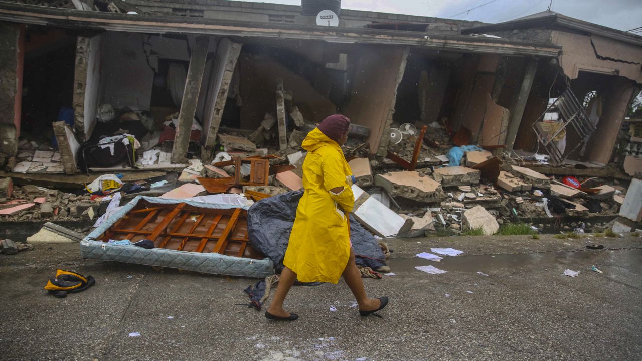 A woman walks in the rain past earthquake-destroyed homes the day after Tropical Storm Grace swept over Les Cayes, Haiti, Tuesday, Aug. 17, 2021, three days after a 7.2-magnitude earthquake hit. (AP Photo/Joseph Odelyn)