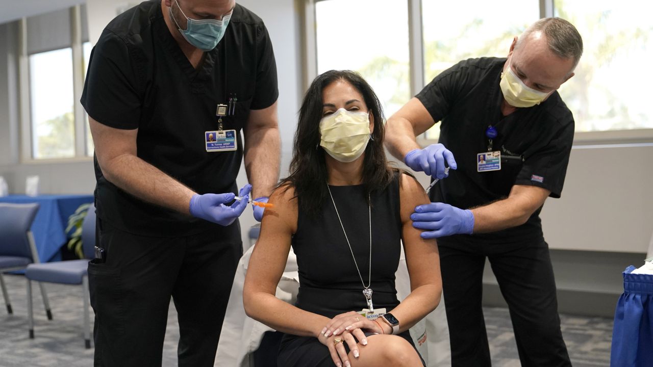 Dr. Lilian Abbo, center, receives a flu vaccine and a Pfizer COVID-19 booster shot at Jackson Memorial Hospital Tuesday, Oct. 5, 2021, in Miami. (AP Photo/Lynne Sladky)