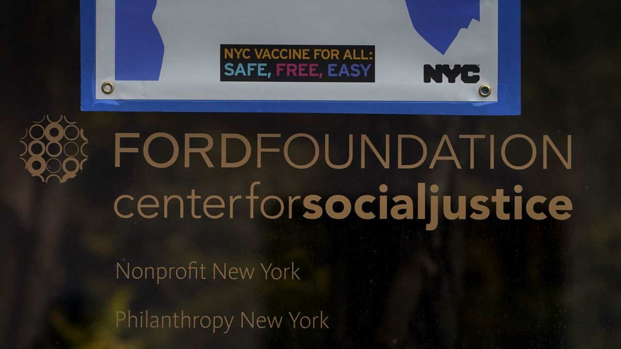 A sign is displayed on a window of the Ford Foundation Building in New York, Friday, Feb. 19, 2021. (AP Photo/Seth Wenig)