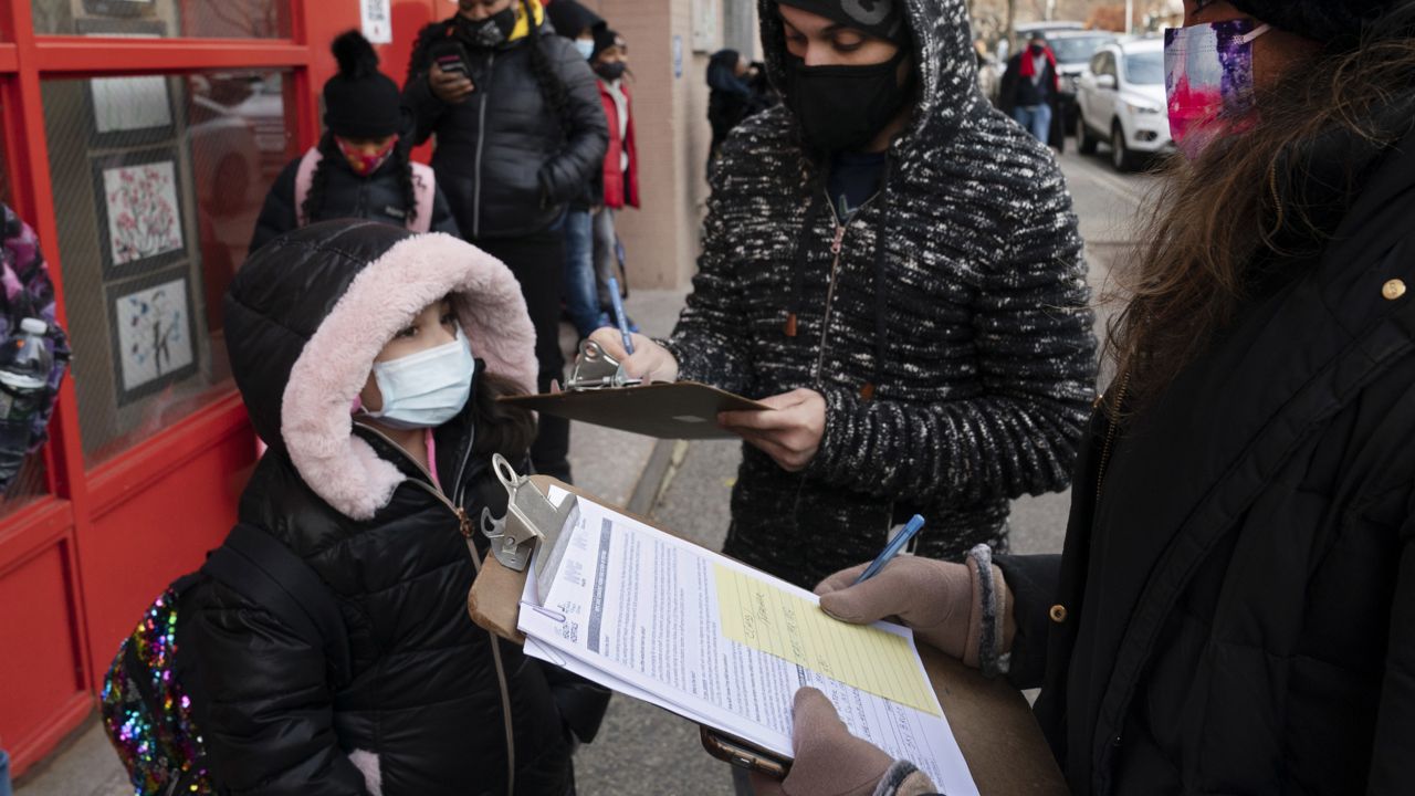 FILE - A parent completes a form granting permission for random COVID-19 testing for students as he arrives with his daughter at P.S. 134 Henrietta Szold Elementary School, in New York on Dec. 7, 2021. (AP Photo/Mark Lennihan, File)