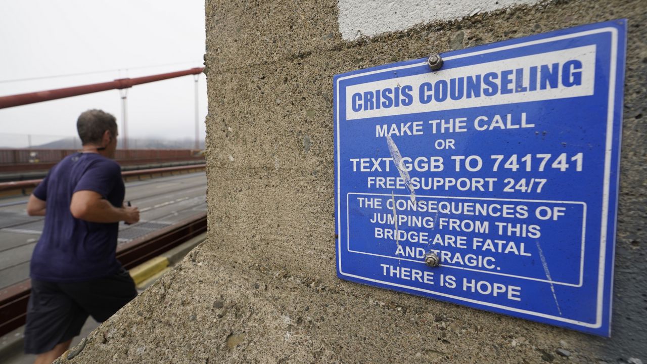 FILE - A man jogs past a sign about crisis counseling on the Golden Gate Bridge in San Francisco, Aug. 3, 2021. (AP Photo/Eric Risberg, File)