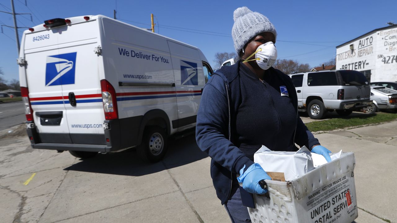 FILE - In this April 2, 2020 file photo, a United States Postal Service worker makes a delivery with gloves and a mask in Warren, Mich. (via Associated Press)