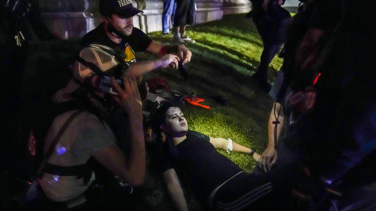 FILE- In this Aug. 25, 2020 file photo, Gaige Grosskreutz, top, tends to an injured protester during clashes with police outside the Kenosha County Courthouse in Kenosha, Wis. Within minutes, Grosskreutz was shot. Prosecutors say 17-year-old Kyle Rittenhouse shot and killed two men during a chaotic protest Aug. 25. They've also accused Rittenhouse of shooting Grosskreutz in the arm. (AP Photo/David Goldman, File)