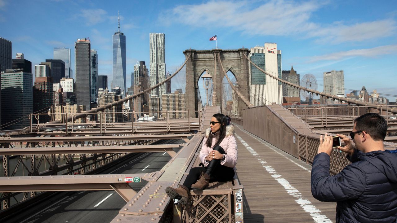 A tourist poses for a picture on the Brooklyn Bridge, March 16, 2020. (AP Photo/Mark Lennihan)