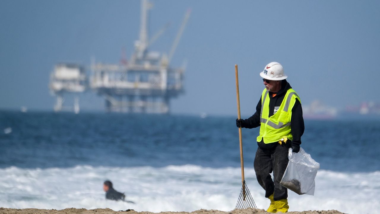 A worker in protective suit continues to clean the contaminated beach in Huntington Beach, Calif., Oct. 11, 2021. (AP Photo/Ringo H.W. Chiu)