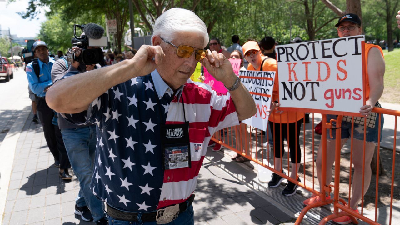 A member of the National Rifle Association plugs his ears with his fingers as he walks past protesters during the NRA's annual meeting at the George R. Brown Convention Center in Houston, Friday, May 27, 2022. (AP Photo/Jae C. Hong)